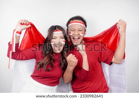 A young Asian couple with a happy successful expression wearing red top and headband while holding Indonesia's flag, isolated by white background. Indonesia's independence day concept. Royalty-Free Stock Photo #2330982641