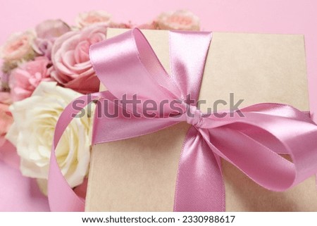 Gift box and beautiful flowers on pink background, closeup