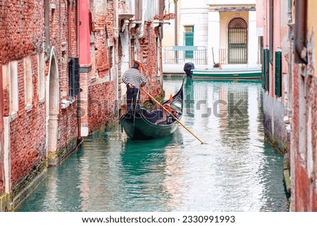 Venetian gondolier punting gondola through green canal waters of Venice Italy Royalty-Free Stock Photo #2330991993