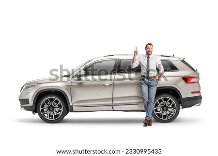 Full length portrait of a man leaning on a SUV and pointing up isolated on white background