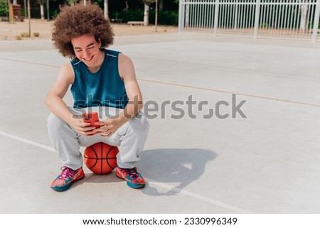 Photo with copy space of a caucasian teen using phone in a basketball court