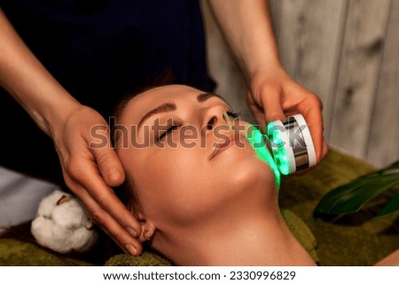 Close-up of beautician hands doing led light therapy to young woman in medical spa salon. Facial phototherapy for skin pore cleaning. Anti-aging treatments and photo rejuvenation procedure. Copy space