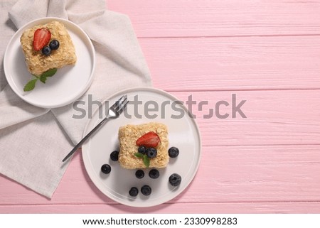 Pieces of delicious Napoleon cake with fresh berries served on pink wooden table, flat lay. Space for text