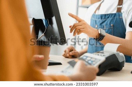 Woman cashier wears an apron and using pos terminal to payment for credit card on coffee shop counter. Royalty-Free Stock Photo #2331003597