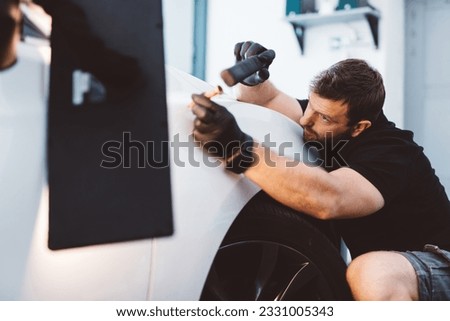 Car mechanic working to remove dent in workshop. Professional car detailing service Royalty-Free Stock Photo #2331005343
