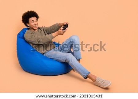 Full body photo of young guy sit beanbag relaxed wear stylish pullover enjoy play video games playstation console isolated on beige color background