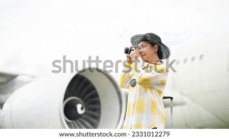A portrait of a happy senior Asian female tourist taking pictures with her film camera at the airport. summer vacation, tourist, trip, holiday