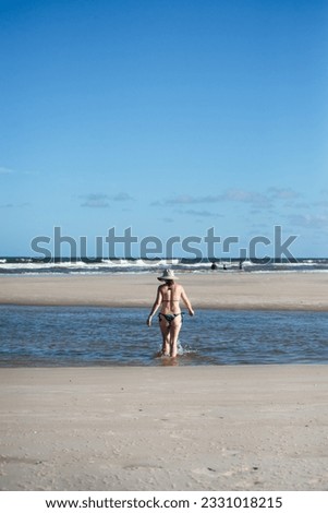 Woman in a bikini and hat entering the water of Taquari, Guaibim beach, Valenca, Bahia.