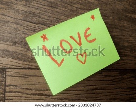 Message written with the word Love on yellow paper, written in English in pink letters, on a wooden background.