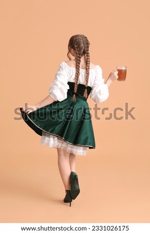 Beautiful Octoberfest waitress with beer dancing on beige background, back view