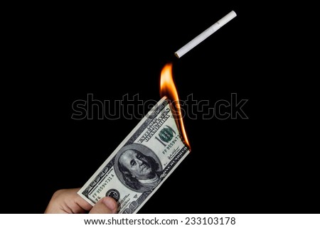 Human hand holding a burning 100 dollar bill and lighting a cigarette