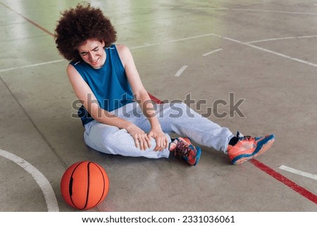 Portrait of a injured basketball player sitting on the floor of a urban court Royalty-Free Stock Photo #2331036061