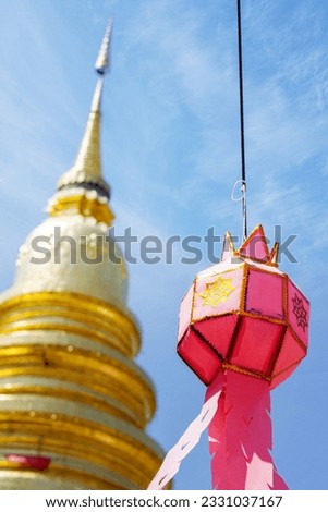 Closeup Thai Lanna style lanterns to hang in front of the golden pagoda at Thai temple under blue sky background.