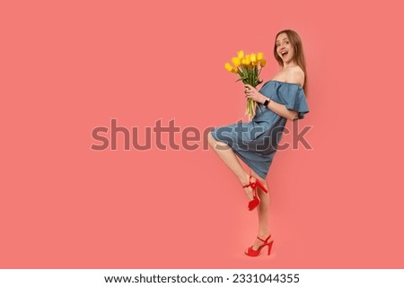 Happy beautiful young woman in gray sundress and red sandals posing in studio with bouquet of tulips. Isolated on pink background. Copy space Royalty-Free Stock Photo #2331044355