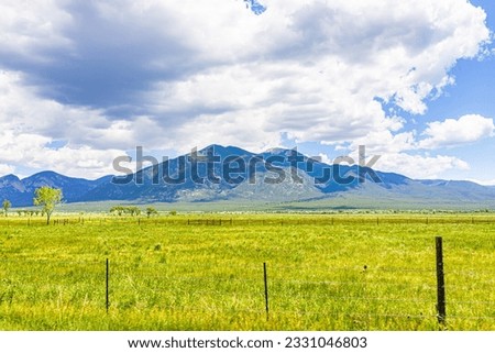 View of Taos Sangre de Cristo mountains and green grass valley landscape in summer with clouds on sunny day in New Mexico