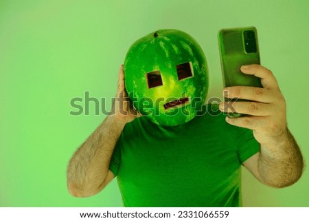 shocked man looking at screen of mobile cell phone, wearing watermelon as helmet, hard hat on head and stylish sunglasses. male isolated on white wallpaper background. bad, breaking news. 