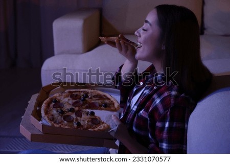Young woman eating pizza while watching TV in room at night. Bad habit Royalty-Free Stock Photo #2331070577