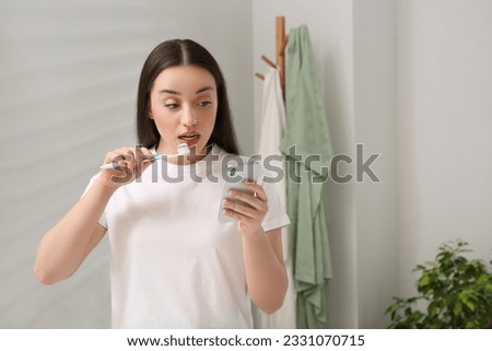 Beautiful young woman using smartphone while brushing teeth in bathroom. Internet addiction Royalty-Free Stock Photo #2331070715
