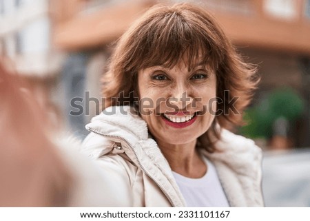 Middle age woman smiling confident making selfie by camera at street