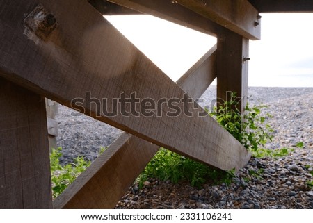 Under a wooden bridge, planks crossing over each other in the sunset at the beach