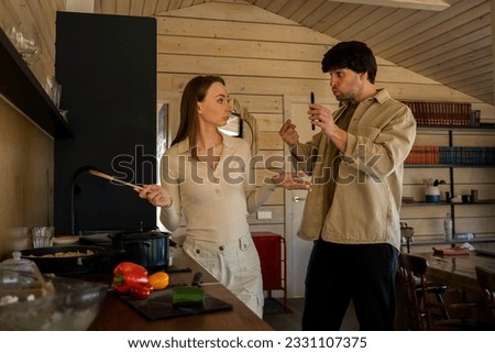 Infidelity. A jealous husband shows his cheating wife her phone, demanding an explanation, standing in the kitchen. Husband caught his wife cheating with a mobile phone - divorcing people.  Royalty-Free Stock Photo #2331107375