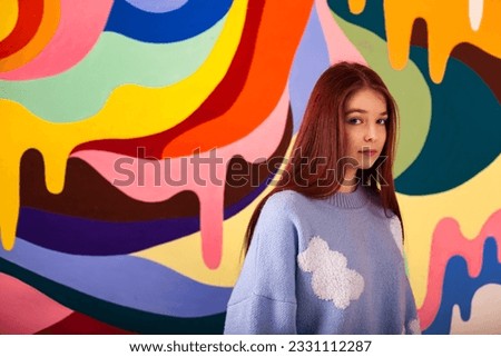 Portrait of lovely teen lady model posing at colored wall, pensive looking at camera. Pretty teenage cover girl in blue fluffy sweater with surprised emotion. Sweet life concept. Copy ad text space