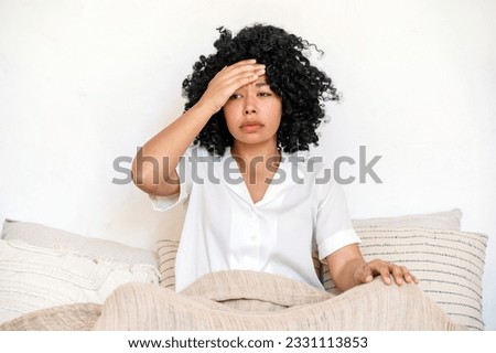 african american woman suffering from headache sitting in bed and touching forehead with hand, feeling unwell and has bad sleep. ill young female awake from fever Royalty-Free Stock Photo #2331113853