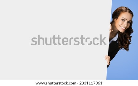 Happy excited woman in black confident suit, peek out showing blank white banner signboard with copy space for sign text. Business and ad concept. Blue color background.