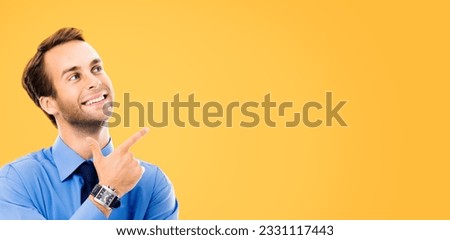 Looking up, smiling businessman pointing showing something, isolated over orange yellow color  background. Business, job and education coach concept. Pointing confident man at studio. Copy space area.