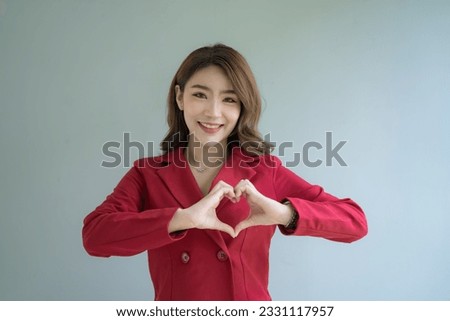 Asian businesswoman in the red suit makes a heart shape with her hands over white background.