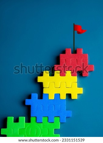 The ultimate goal, red flag on top of colorful puzzle blocks as bar graph chart steps on blue background, minimal style. Business growth process, winner, opportunity and great aspiration concepts.