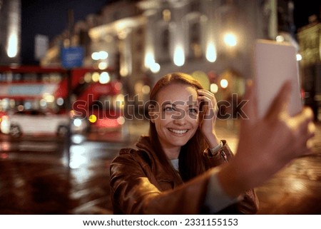 Young woman taking a selfie at night while walking in the city london