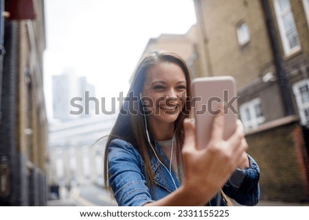 Young woman using a smart to take a selfie while walking in london