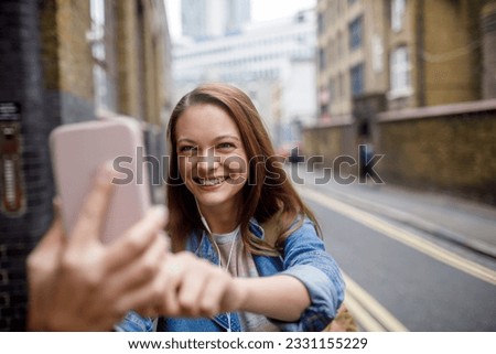 Young woman using a smart to take a selfie while walking in london
