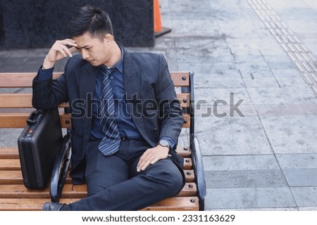 Asian young businessman stress sitting on bench in front office with his hands touching his head. Top view
