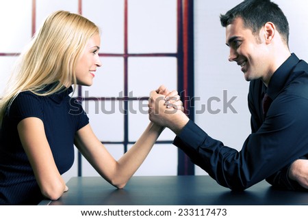 Young happy couple or business people fighting in arm-wrestling