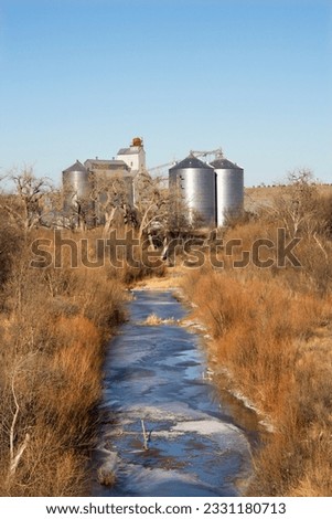 Storage silos by creek in rural setting.
