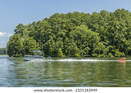 Pontoon boat pulling inflatable tube float raft on lake. Family on a pontoon party boat enjoying tubing on a summer day with their children. Royalty-Free Stock Photo #2331183949