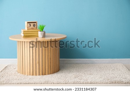 Coffee table with books, cube calendar and houseplant near blue wall