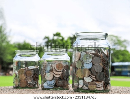Coins in glass jar with blurred green trees background, concept of money savings      