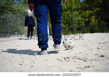 The guy kicks the soccer ball into the goal on the sand. Close-up from ground