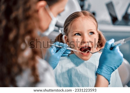 Children's dentistry. First examination at the dentist. A cute beautiful girl with an open mouth is looking to the side while the doctor is treating her teeth. Royalty-Free Stock Photo #2331223593