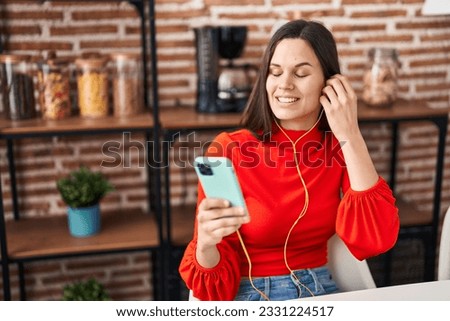 Young beautiful hispanic woman listening to music sitting on table at home