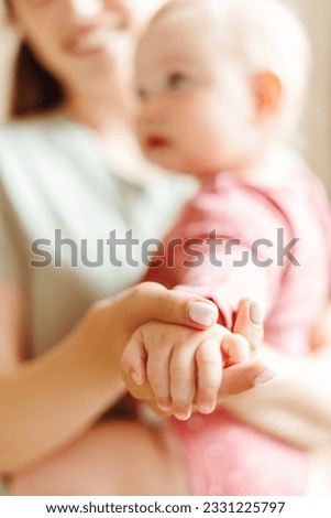 Attractive, smiling woman holding small beautiful baby, selective focus on baby's hand. Positive female with child. Love, care, parenthood concept Royalty-Free Stock Photo #2331225797