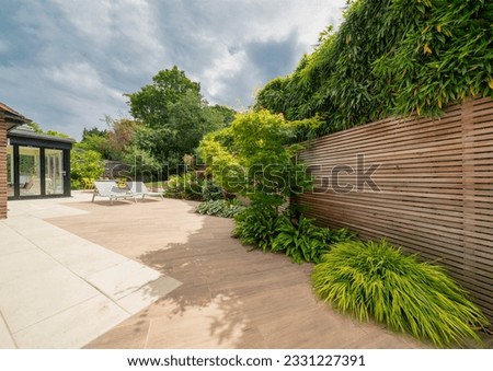 View of stylish, luxury, designer patio and garden with loungers and plants on sunny, summer day.