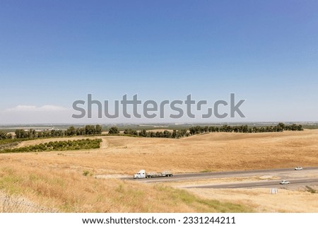 Highway in California, on which cars and trucks drive, among the yellow grass on a sunny day. American landscape from a bird's eye view. Vacation trip