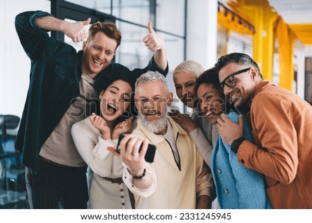 Adult male corporate director using cellphone media application for clicking selfie photo with friendly office team of employees, cheerful group of professional colleagues smiling and shooting video