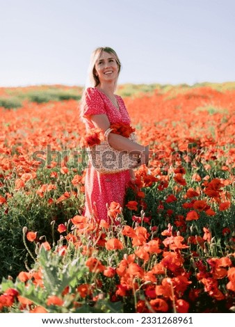 Attractive caucasian woman at a flowered poppy field. Smiling woman in dress and straw handbag with red flowers