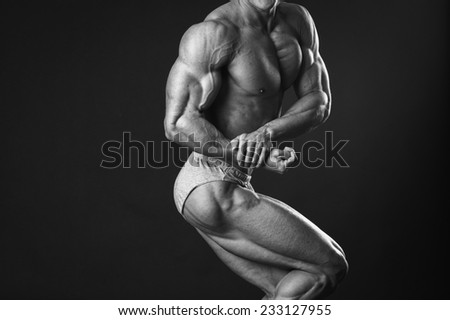 Black and white photography. Handsome muscular guy, bodybuilder, posing on a black background. Traced muscles, posing, sports, muscle power - the concept of sport of bodybuilding.