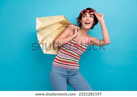 Photo of charming excited woman dressed tank top dark eyewear rising shoppers looking empty space isolated blue color background